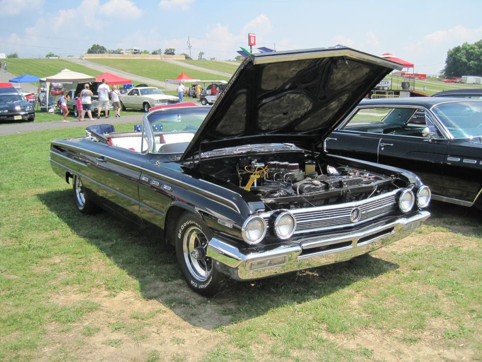 Black convertible with hood open, front view. Another black car is parked beside it