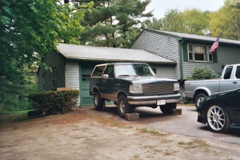 1994 Ford Bronco - A dark green Ford Bronco is parked in front of a garage, with two other vehicles visible.