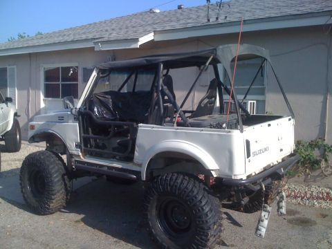 1987 Suzuki Samurai - This modified Suzuki Samurai features oversized tires and a roll cage, parked in front of a house.