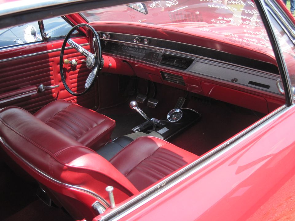Red interior of a classic car, showing front seats, dashboard, steering wheel, and gear shifter