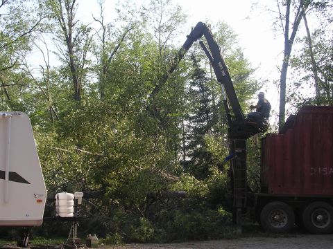 1978 Ford Bronco - A man operates a crane from a basket, working near a dump truck and a trailer in a wooded area.