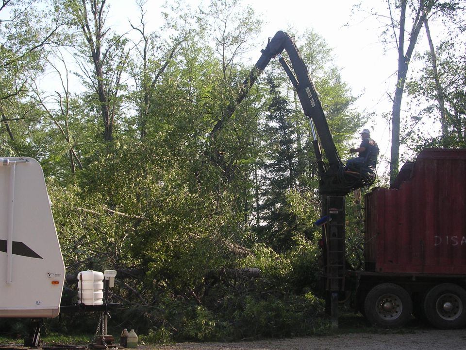 Crane truck with man in basket next to a red dump truck and a white trailer