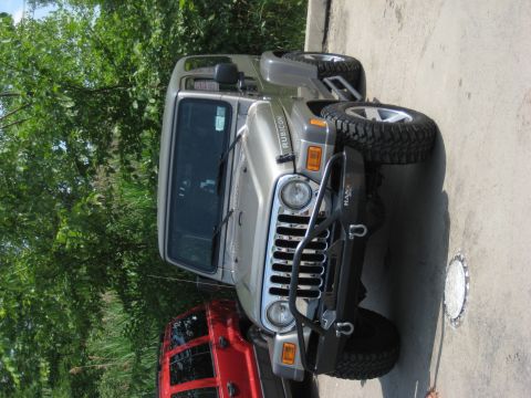 2005 Jeep Wrangler - A silver 2005 Jeep Wrangler Rubicon is parked outdoors, partially obscured by trees and another vehicle.