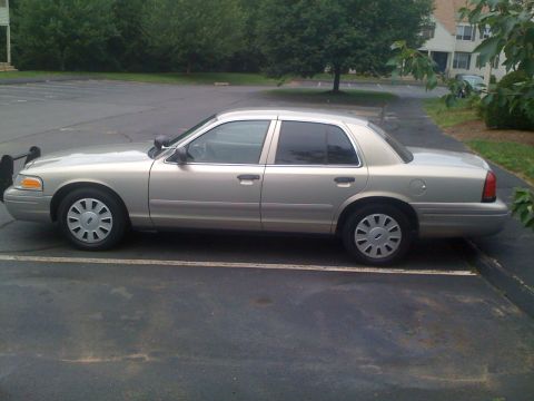 2009 Ford Crown Victoria - A tan Ford Crown Victoria is parked in a lot, showing its side profile and a push bumper.