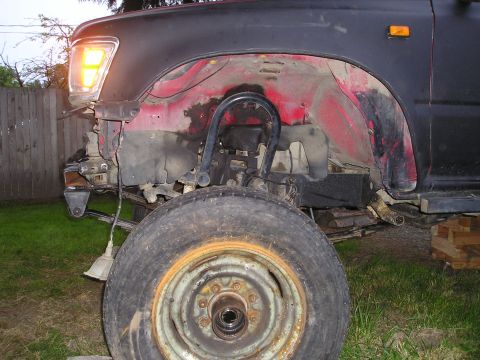 1990 Toyota Pickup/SR5 - Front passenger side suspension and wheel well of a 1990 Toyota Pickup/SR5, showing the red inner fender and black fender flare.
