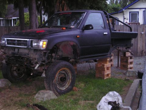 1990 Toyota Pickup/SR5 - This Toyota pickup truck is elevated on wooden blocks, with its front bumper removed and a roll bar installed in the bed.