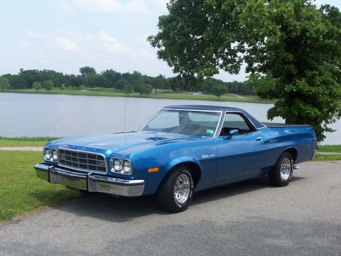 1973 Ford Ranchero - A blue 1973 Ford Ranchero sits parked near a body of water under a large tree.