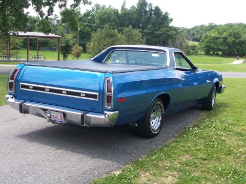 1973 Ford Ranchero - Rear view of a blue 1973 Ford Ranchero pickup truck parked on a paved surface with a grassy area and trees in the background.