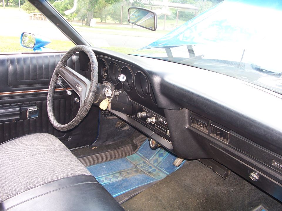 1973 Ford Ranchero interior showing dashboard, steering wheel, and seats. Blue floor mats have 'FORD' logo