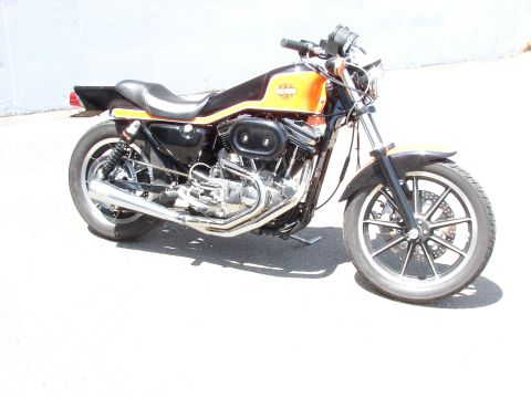 1993 Jeep YJ - A Harley-Davidson Sportster motorcycle is parked on a paved surface with a white wall in the background.