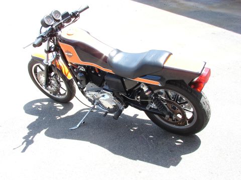 1993 Jeep YJ - A parked motorcycle displays its orange and brown fuel tank and black seat under a bright sky.