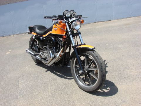 1993 Jeep YJ - A motorcycle with an orange fuel tank and black bodywork is parked outdoors on a paved surface.
