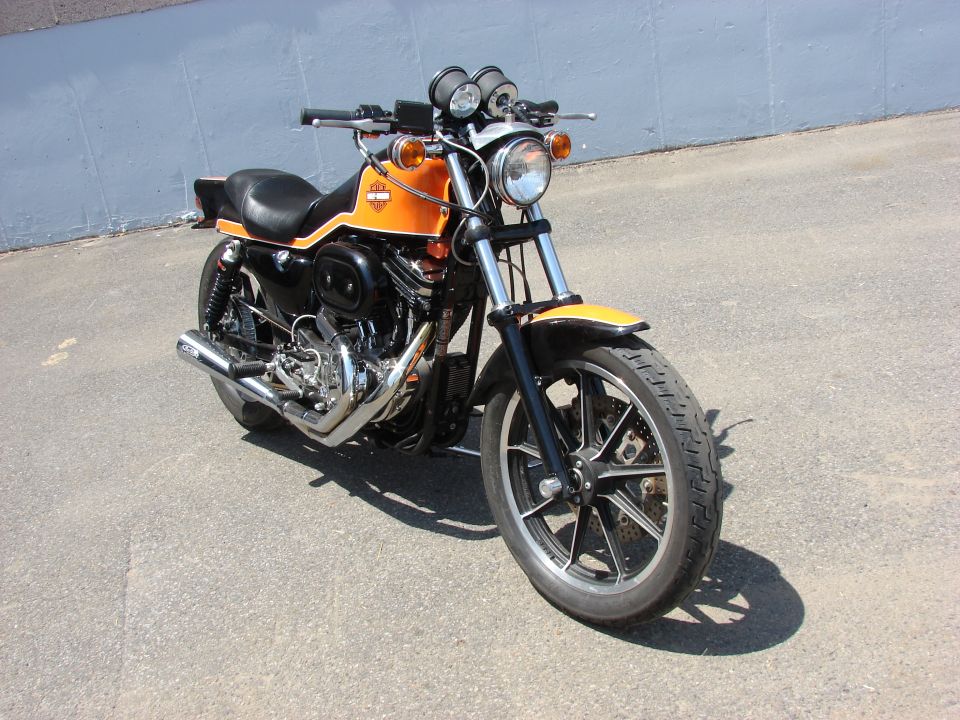 Orange and black motorcycle parked on pavement, front wheel and engine visible