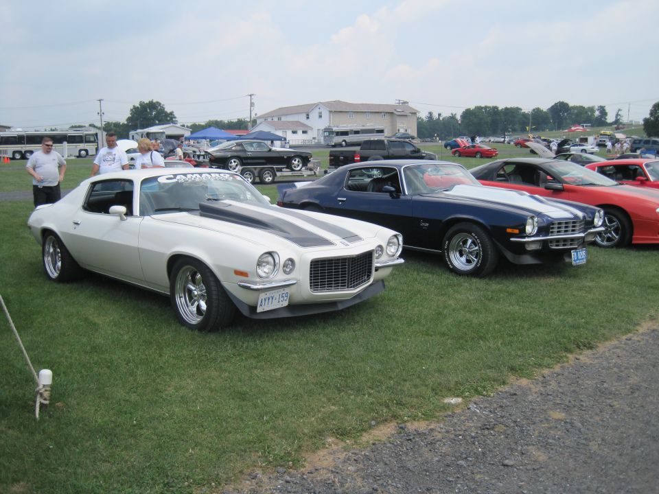 White 1970 Chevrolet Camaro with black racing stripes and a hood scoop, parked on grass