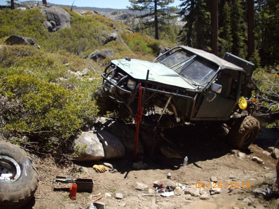 Off-road vehicle tilted on rocks with a jack and tools nearby