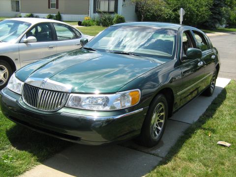 1988 Mercury Grand Marquis - A green sedan is parked on a driveway next to another car.