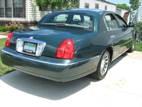1988 Mercury Grand Marquis - A green sedan is parked on a concrete driveway in front of a house.