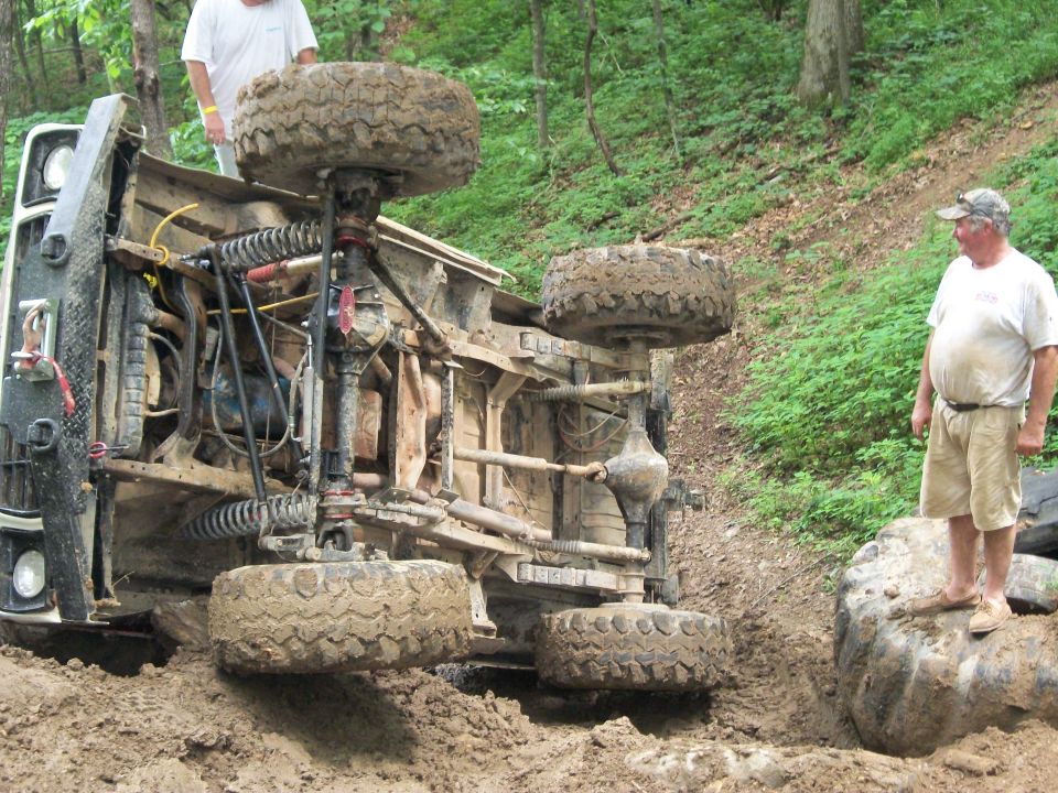 Off-road vehicle flipped onto its side in mud with two men standing nearby