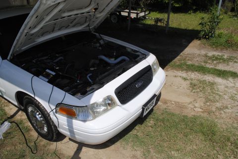 2002 Ford Crown Victoria - A white 2002 Ford Crown Victoria is parked outside with its hood open, revealing the engine compartment.
