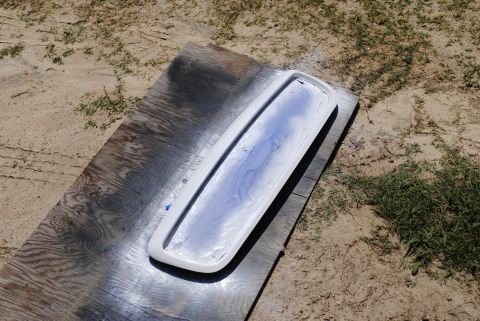 2002 Ford Crown Victoria - A vehicle grille is being spray painted white, with blue paint visible on the surface and surrounding plywood.