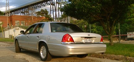 2000 Ford Crown Victoria - Rear view of a silver 2000 Ford Crown Victoria sedan parked near a tree and a bridge structure.