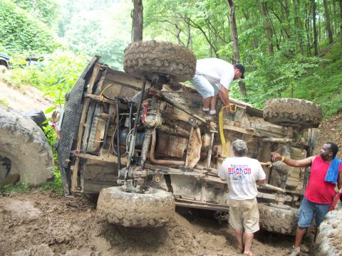 1978 Ford Bronco - This off-road vehicle is on its side in the mud, with several people attempting to assist.