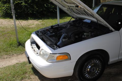 2002 Ford Crown Victoria - The front of a white 2002 Ford Crown Victoria is shown with its hood raised, revealing the engine compartment.