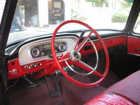 1966 Ford F-100 - Interior of a classic pickup shot through the open driver's door, showing a large red three-spoke steering wheel with chrome horn ring, a r…