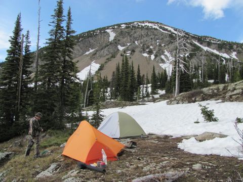 1974 Ford Ranchero - Campsite in a mountainous area with snow patches and evergreen trees, two tents and a person.