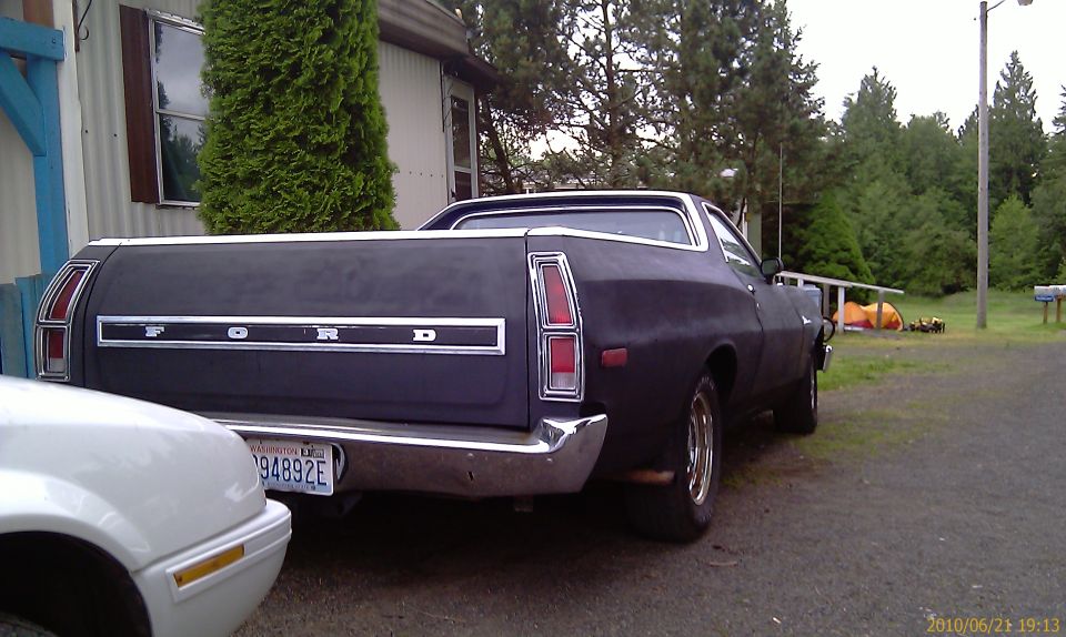 Dark 1976 Ford Ranchero's rear end, parked next to a white car. License plate reads 94892E