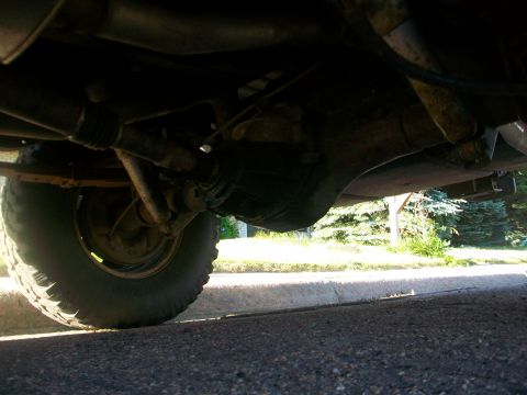 1986 Ford Bronco - A low-angle shot reveals the underside of a vehicle, focusing on the rear axle assembly and a portion of the tire.