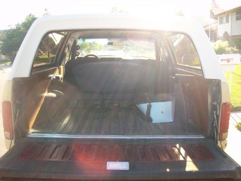 1986 Ford Bronco - The open tailgate reveals the cargo area of a 1986 Ford Bronco, showing its interior and the surrounding suburban environment.