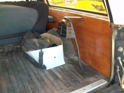 1986 Ford Bronco - The rear cargo area of a vehicle shows wooden paneling and a seat covered by a protective cloth.