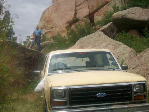 1986 Ford Bronco - 1986 Ford Bronco parked in a natural, rocky landscape with people observing.
