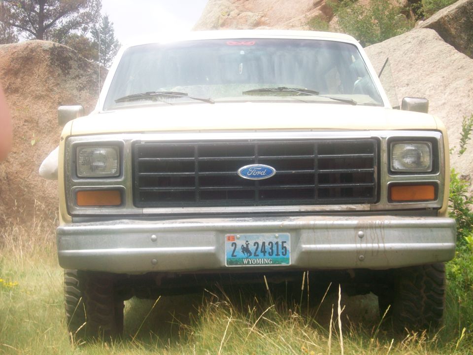 Front view of a tan Ford Bronco parked in a grassy, rocky area. License plate reads '2 24315 WYOMING'