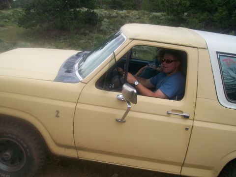 1986 Ford Bronco - Man driving a yellow Ford Bronco, likely from the 1980s, with a white hardtop.