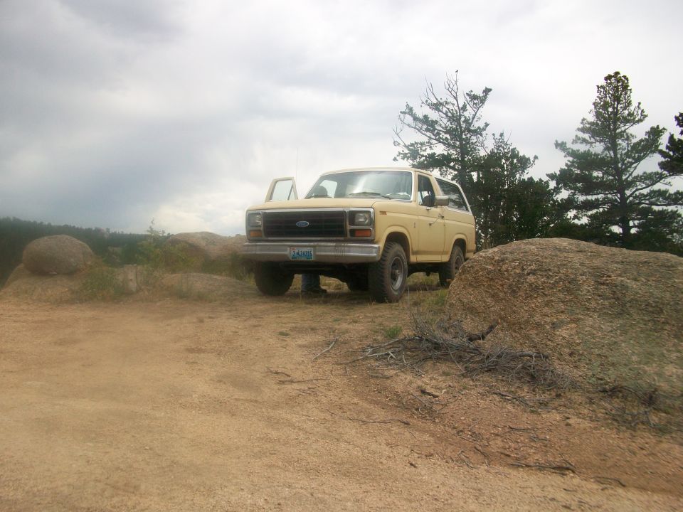 Yellow Ford Bronco parked on dirt road near rocks and trees