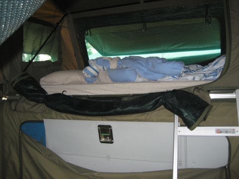 1996 Ford Bronco - The interior of a pop-up camper tent shows a bed with bedding and pillows, ready for use.