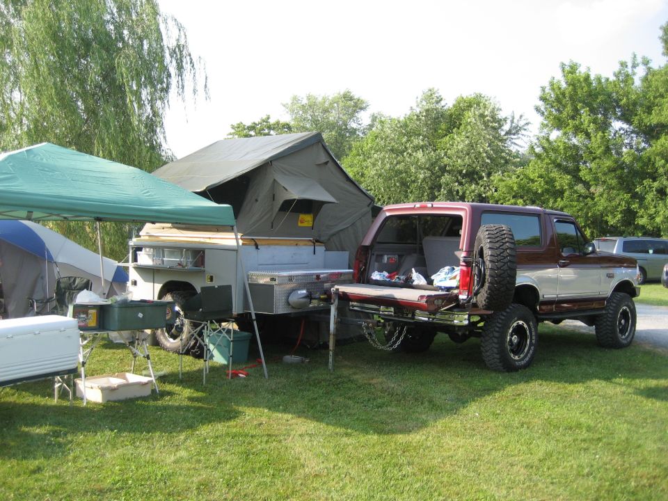 Red and silver SUV with pop-up camper trailer, rear view. Spare tire mounted on back