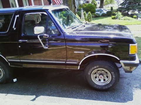 1990 Ford Bronco - Side profile of a black 1990 Ford Bronco, chrome accents and alloy wheels.
