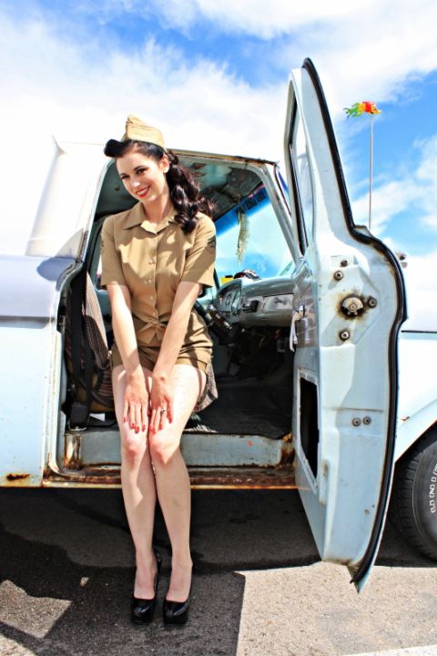 1963 Ford F-100 - A woman in a vintage military-style outfit poses next to the open door of a classic pickup truck.