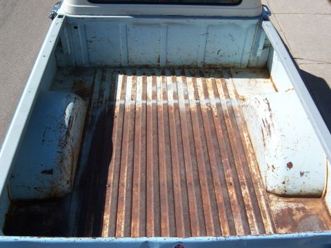 1963 Ford F-100 - The interior of a light blue pickup truck bed shows significant rust on its floor and wheel wells.