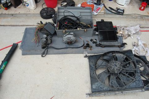 1994 Ford Bronco - Various automotive parts are laid out on a mat, including an alternator, radiator, and fan assembly.