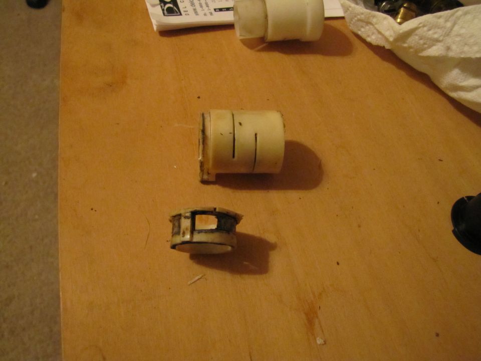 Two white plastic clutch linkage parts on a wooden surface. One is cylindrical with slits, the other is a shorter, rectangular piece