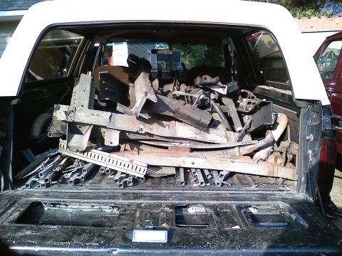 1990 Ford Bronco - Rear view into a dark-blue full-size SUV with a white removable top, tailgate down and glass raised, loaded to the roof with scrap steel: r…