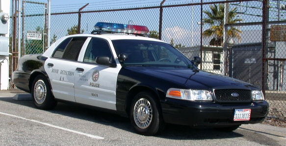 Black and white police Ford Crown Victoria parked by a chain-link fence