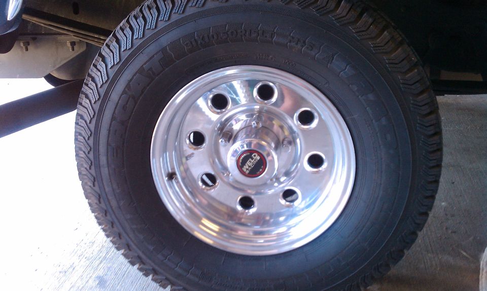 Chrome Weld wheel with black lug nuts on a tire. Part of a vehicle frame is visible above