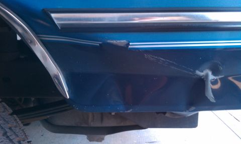 1992 Ford Bronco - The lower body panel of a blue vehicle displays damage and a detached piece of trim.