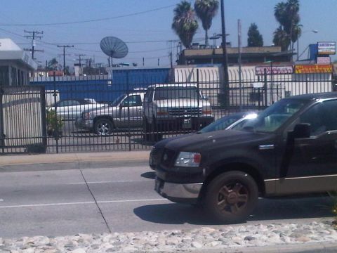 1986 Ford Bronco - A black Ford F-150 truck is parked in front of a fence with other vehicles behind it.