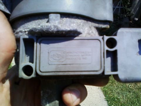 1990 Ford Bronco - Sunlit close-up of a gray TFI ignition module still bolted to a distributor held in a hand, with the molded case text reading 'Manufactured…